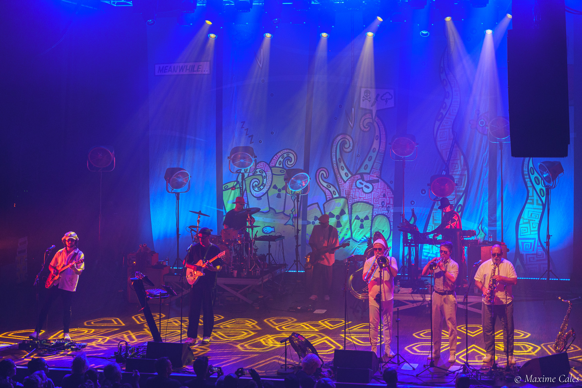 Fat Freddy's Drop au complet avec sa section cuivres devant le décor illustré, concert au Bikini